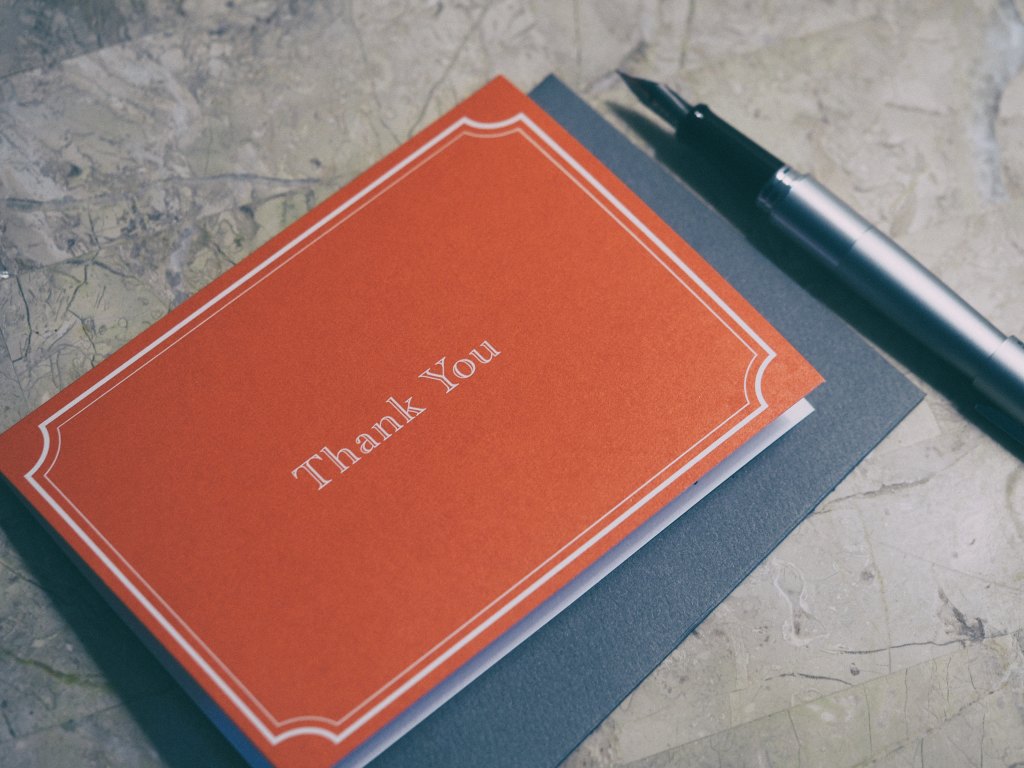 Red card with the words "thank you" on it next to a fountain pen.