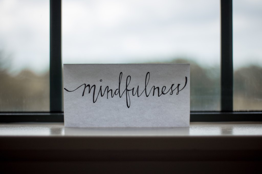 A piece of paper with the word "mindfulness" on it leaning against a window
