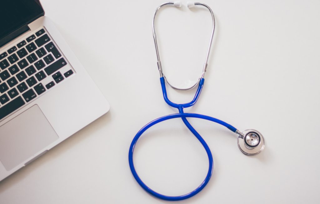 Stethoscope next to a laptop on a white surface.
