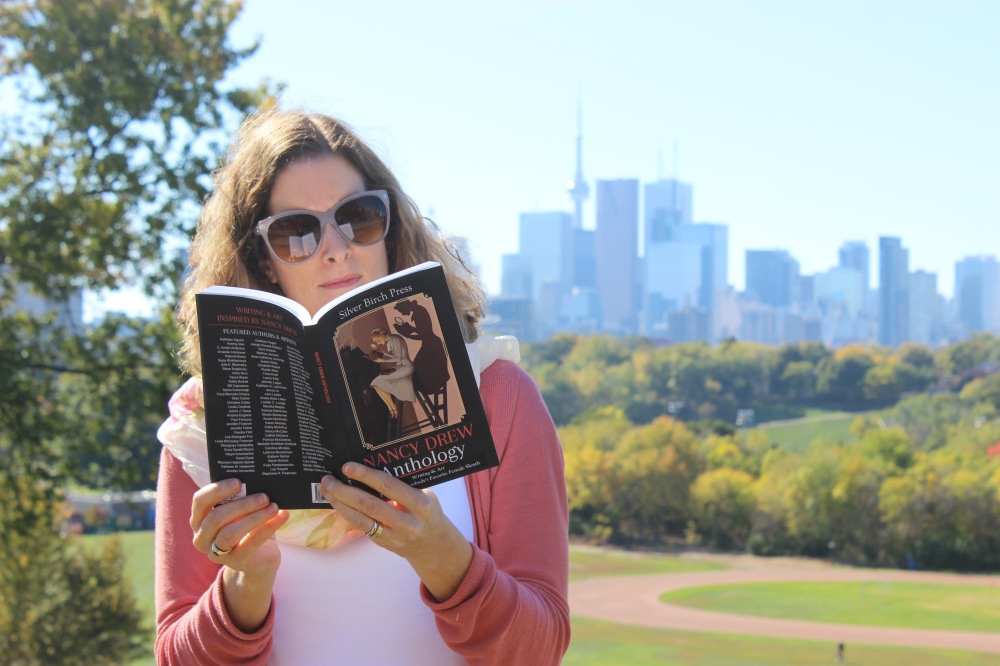Photo of Lee Parpart reading a book with the Toronto skyline in the background.