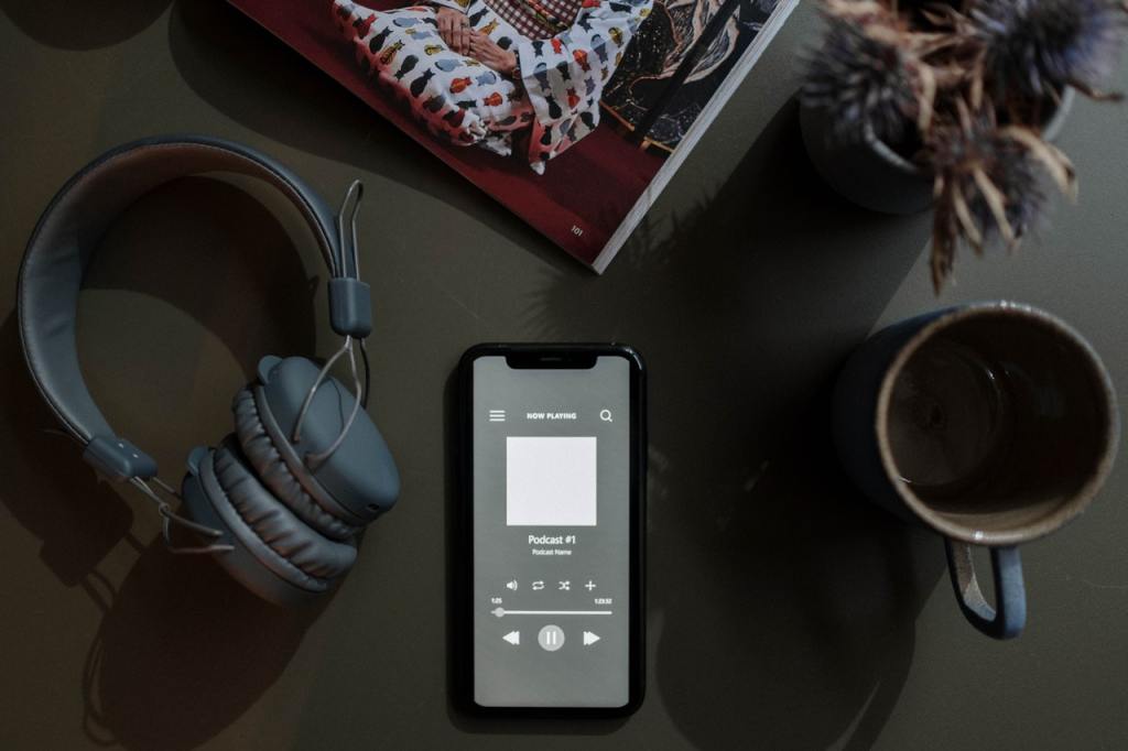 Photo of a smartphone with a podcast playing, with a set of headphones on the left and a mug of coffee on the right.