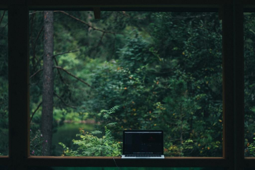 Image of a laptop placed on a porch, with a view of trees in the background.