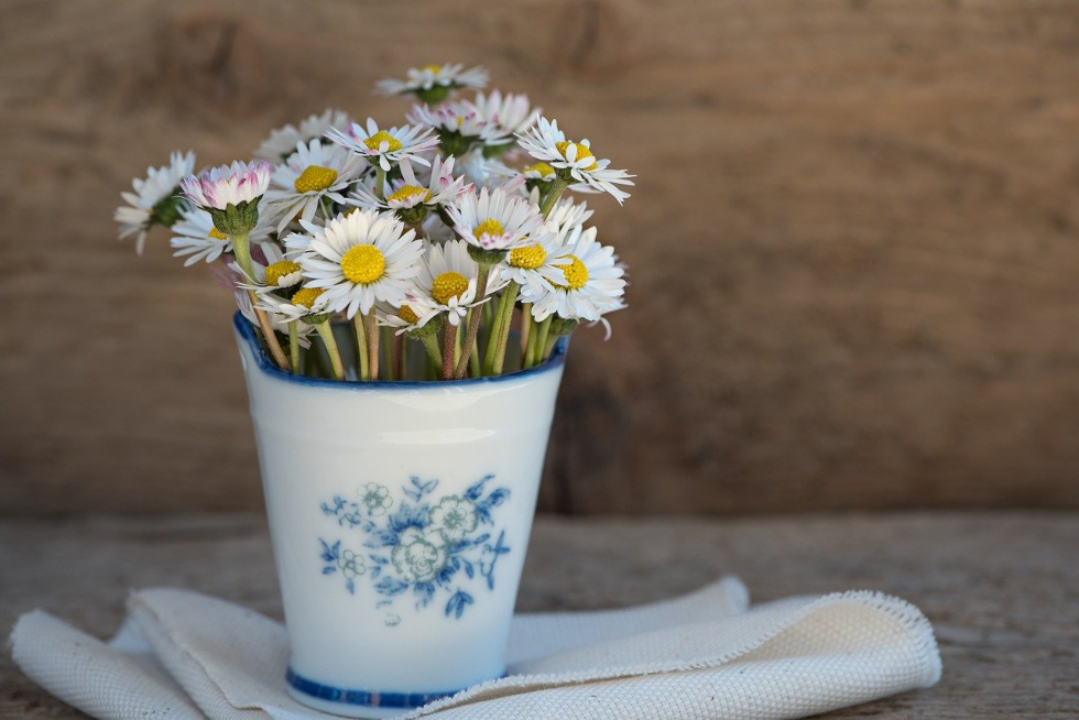 A buquet of daisies in a bucket-shaped vase on a rough wood table.