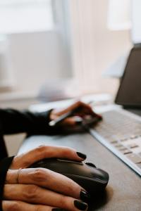 A hand is seen on a desk, moving a keyboard mouse. 