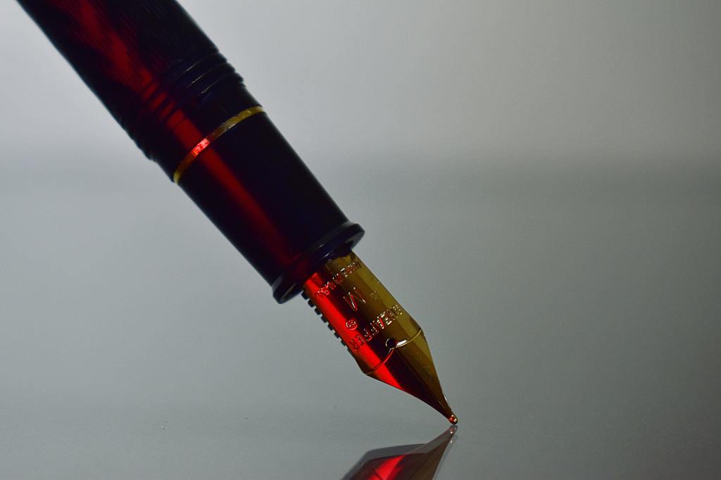 A close-up of a pen with its tip poised on a clear reflective surface, ready to write.