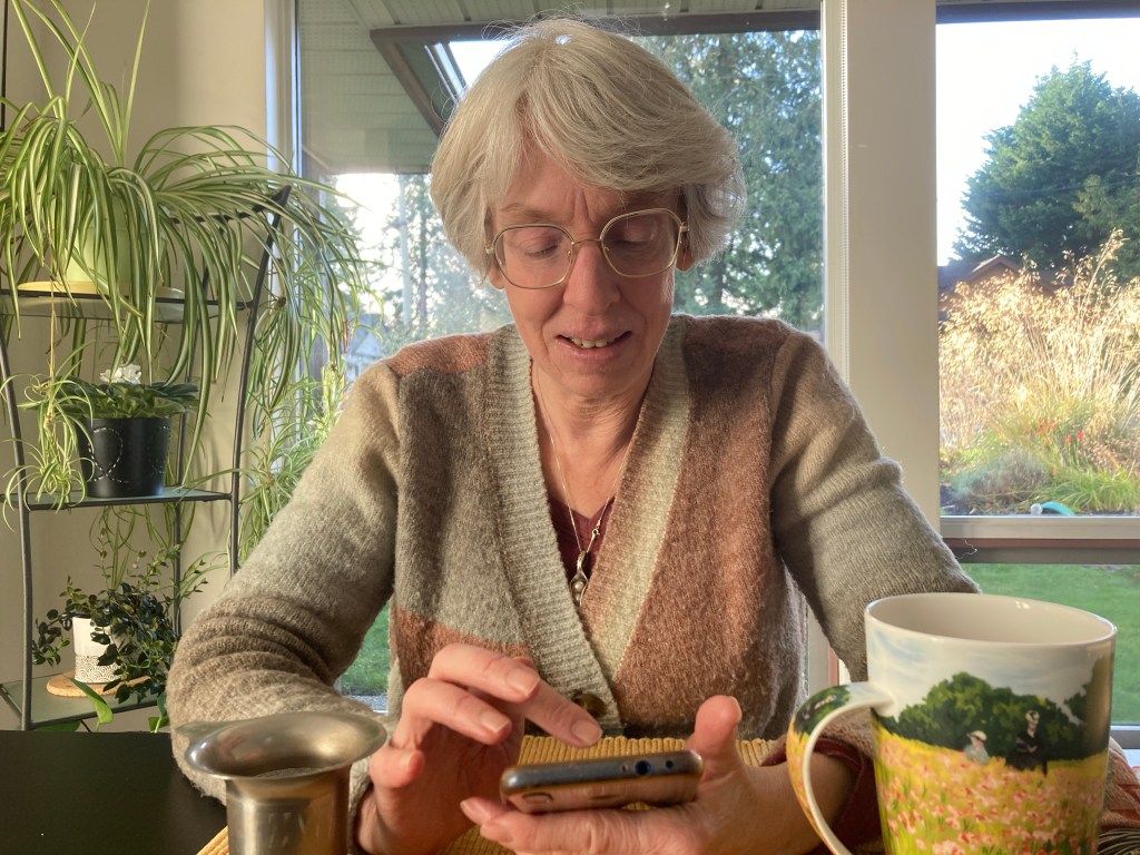 Lenore Hietkamp sits at a table with foliage in the background.