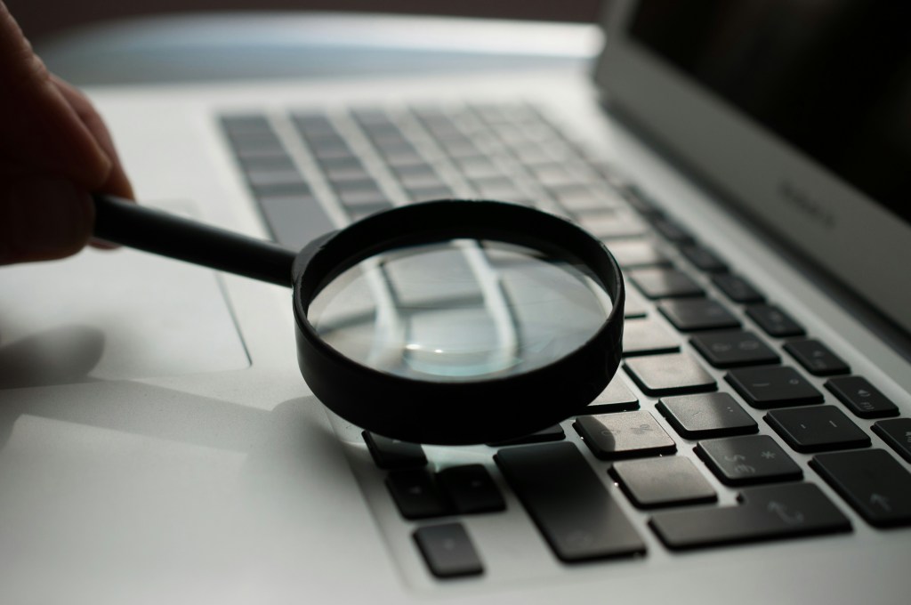 A magnifying glass is held on a laptop's keyboard.