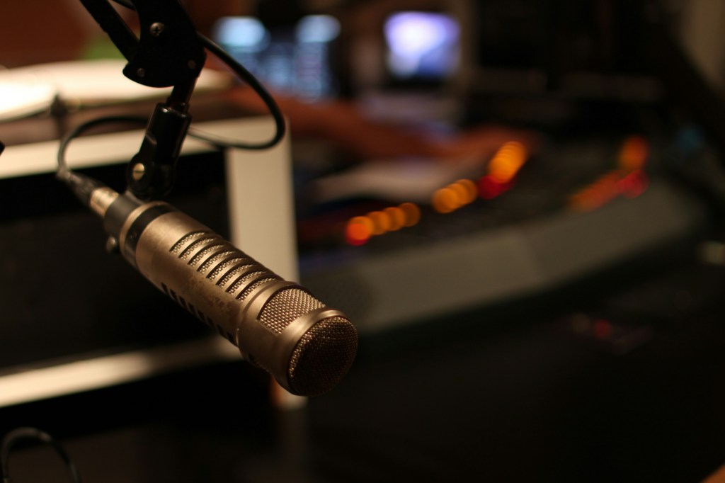 A microphone hangs in front of a blurred background of a recording studio.