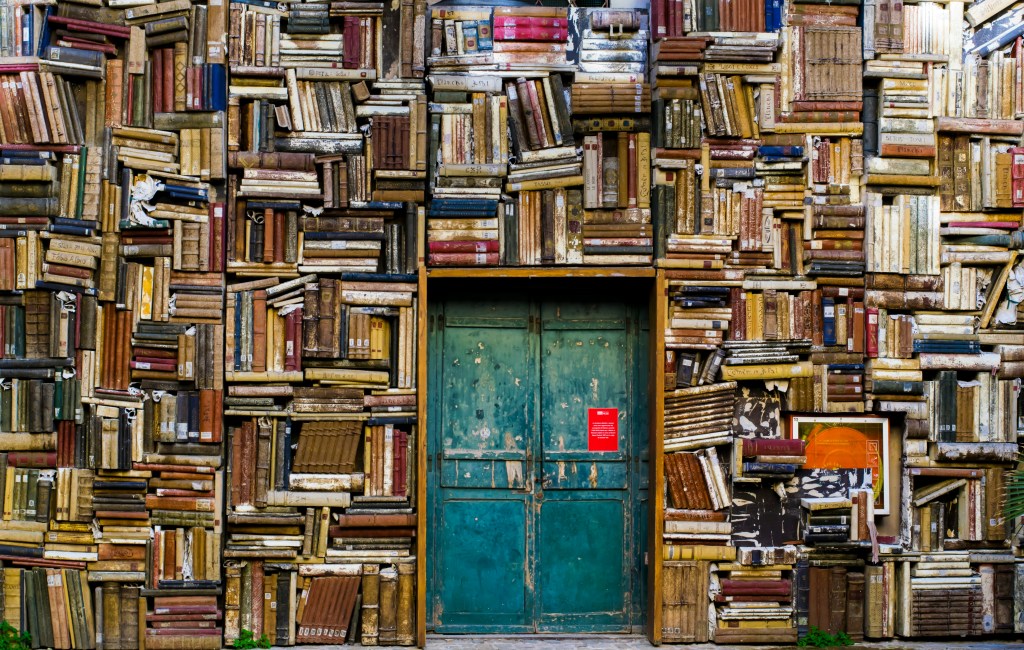 A blue-green door surrounded by many shelves and many stacks of books.