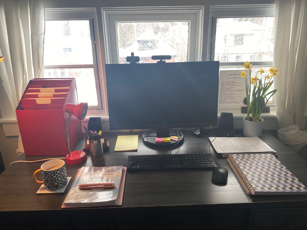 Workspace with desk, computer, notebooks, and coffee.