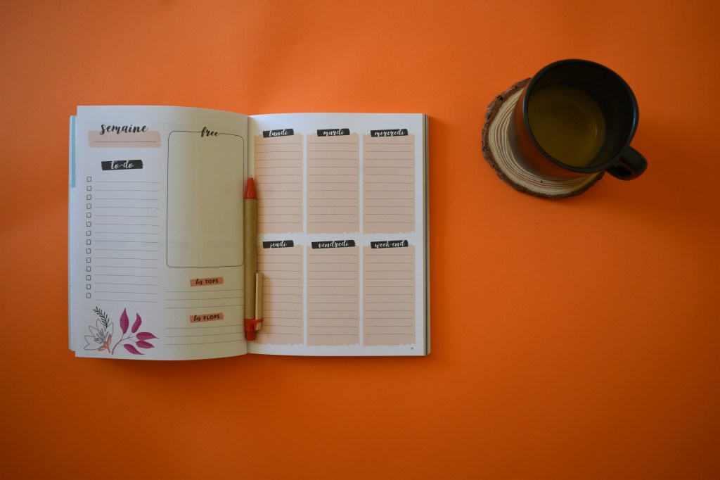 A French weekly planner and cup of coffee on an orange background.