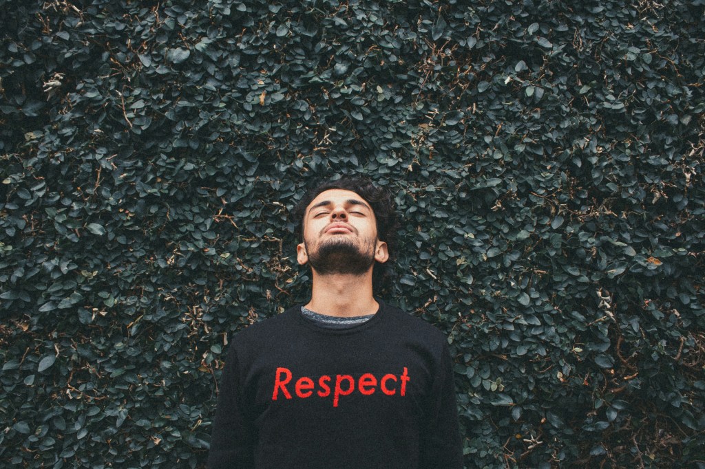 A person standing in front of a hedge, wearing a sweater with the word "Respect".