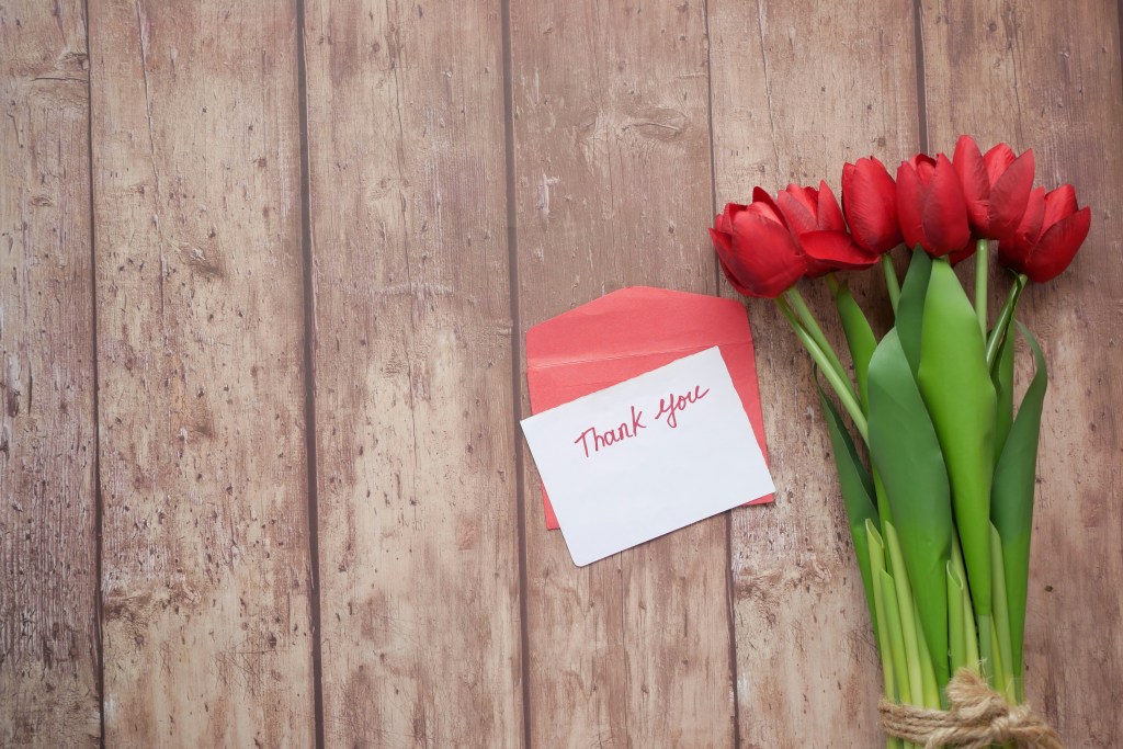 A bunch of red tulips and a thank-you card on a background of wood.